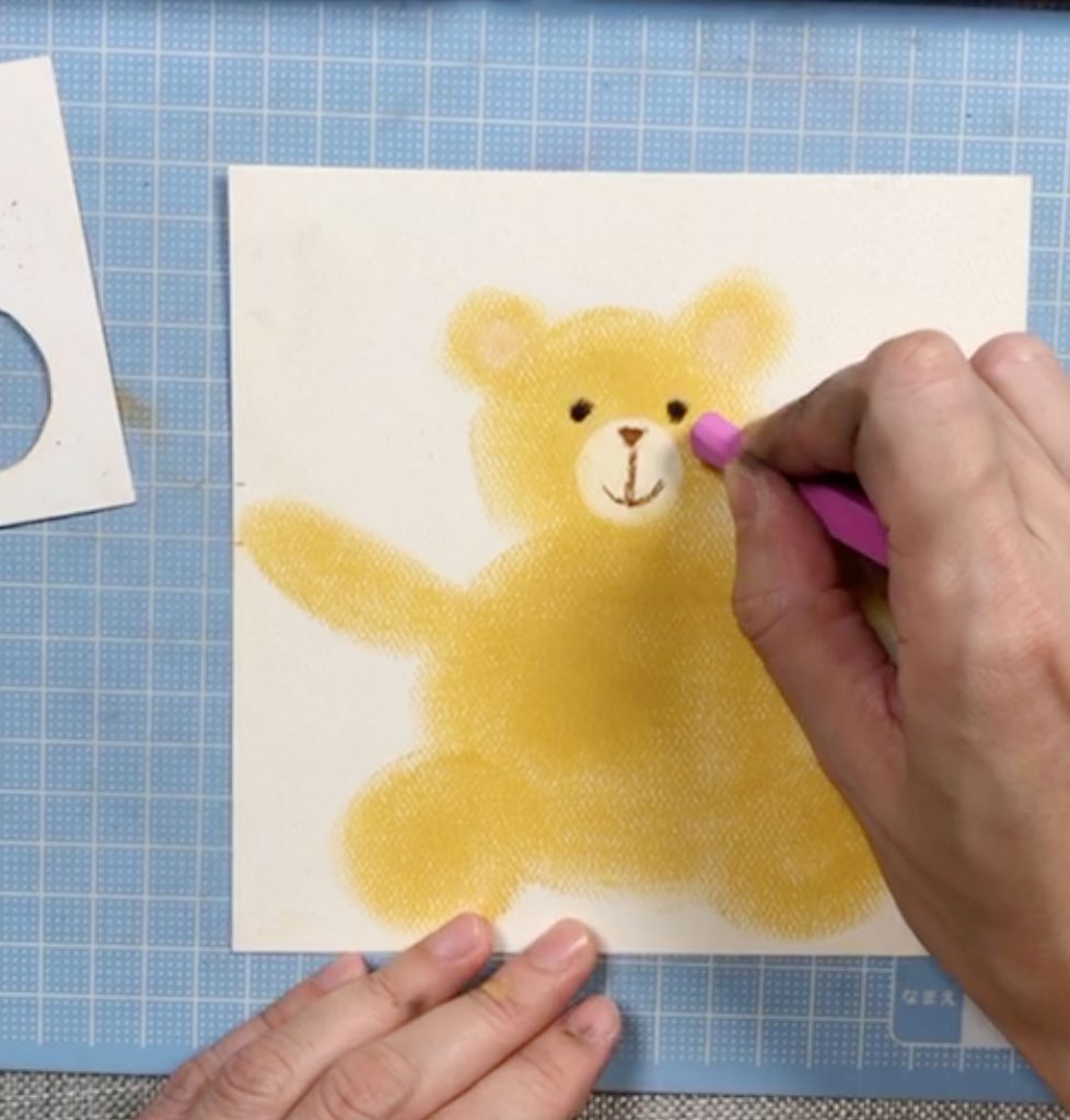 用乾粉彩直接在畫紙上畫出熊仔的眼、鼻、嘴和胭脂